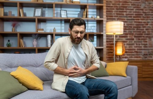 stock-photo-a-young-man-feels-severe-stomach-pain-spasms-poisoning-discomfort-sitting-on-the-sofa-at-home-2266543079